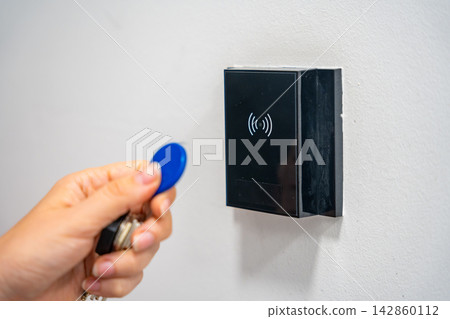 Person using contactless key fob on indoor access control reader. Secure building access protects restricted areas and residential facilities Person using contactless key fob on indoor access control reader. Secure building access protects restricted areas and residential facilities 142860112