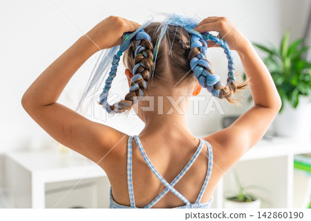 Little girl showing blue braided hair extensions from the back while playing with colorful hairstyle. Childhood creativity and Generation Alpha self expression celebrate playful beauty trends Little girl showing blue braided hair extensions from the back while playing with colorful hairstyle. Childhood creativity and Generation Alpha self expression celebrate playful beauty trends 142860190