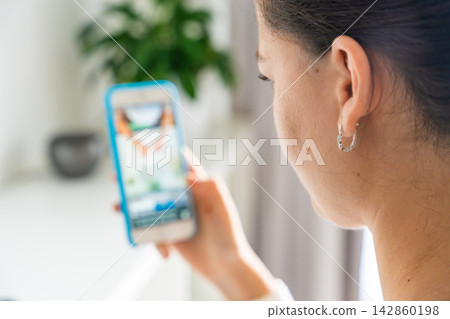 Woman scrolling social media on a smartphone at home. Digital addiction concept with endless content consumption and screen time. Woman scrolling social media on a smartphone at home. Digital addiction concept with endless content consumption and screen time. 142860198