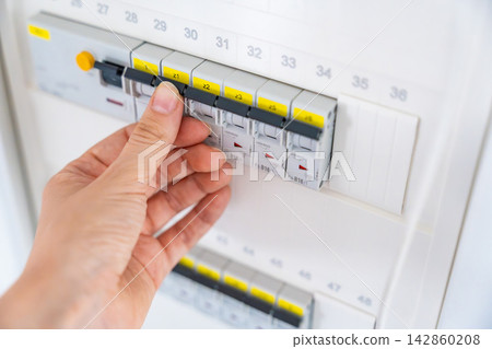 Hand operating an electrical circuit breaker in a residential distribution board. Electrical safety and power management support maintenance, energy efficiency, and infrastructure reliability. Hand operating an electrical circuit breaker in a residential distribution board. Electrical safety and power management support maintenance, energy efficiency, and infrastructure reliability. 142860208