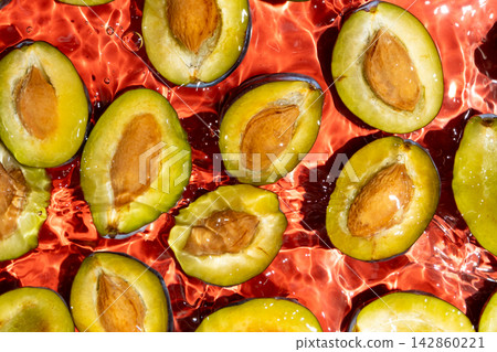Fresh plum halves with pits floating in clean water overhead view Fresh plum halves with pits floating in clean water overhead view 142860221