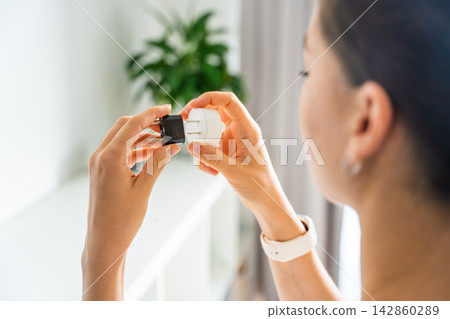 Woman compares electrical plug adapters for different power outlets at home. International travel and power compatibility concept for global electronics. Woman compares electrical plug adapters for different power outlets at home. International travel and power compatibility concept for global electronics. 142860289