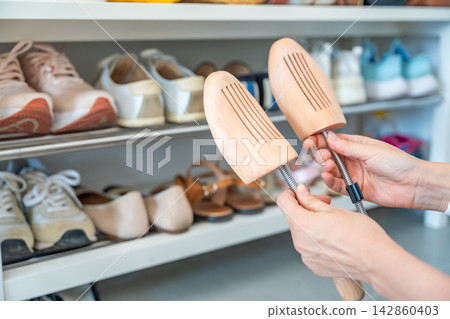 Hands adjusting a pair of wooden shoe trees before use. Regular footwear maintenance protects leather shoes and extends durability. Hands adjusting a pair of wooden shoe trees before use. Regular footwear maintenance protects leather shoes and extends durability. 142860403