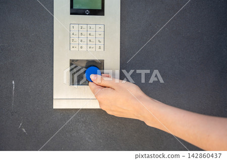Person using contactless key fob on residential building access control system. Secure entry technology supports convenient and controlled property access Person using contactless key fob on residential building access control system. Secure entry technology supports convenient and controlled property access 142860437