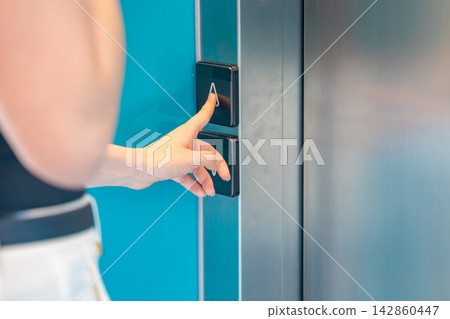 Person pressing elevator call button in modern residential building. Everyday accessibility and vertical transportation improve convenience and mobility Person pressing elevator call button in modern residential building. Everyday accessibility and vertical transportation improve convenience and mobility 142860447
