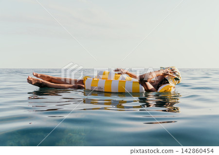 Man Float Ocean - Relaxing on a yellow and white striped inflatable float in the ocean on a sunny day. Man Float Ocean - Relaxing on a yellow and white striped inflatable float in the ocean on a sunny day. 142860454