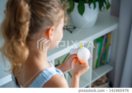 Child squeezes a soft squishy stress relief toy at home. Sensory play supports emotional regulation, relaxation and focus through tactile interaction. Child squeezes a soft squishy stress relief toy at home. Sensory play supports emotional regulation, relaxation and focus through tactile interaction. 142860476