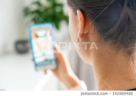 Woman scrolling social media on a smartphone at home. Digital addiction concept with endless content consumption and screen time. 142860480