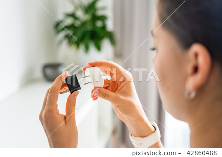 Woman compares electrical plug adapters for different power outlets at home. International travel and power compatibility concept for global electronics. Woman compares electrical plug adapters for different power outlets at home. International travel and power compatibility concept for global electronics. 142860488