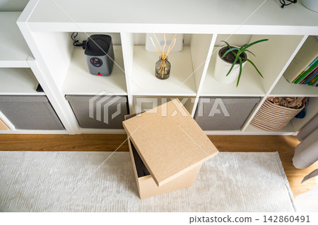 Fabric storage box slightly pulled out from shelf in modern home interior. Home organization and decluttering concept Fabric storage box slightly pulled out from shelf in modern home interior. Home organization and decluttering concept 142860491