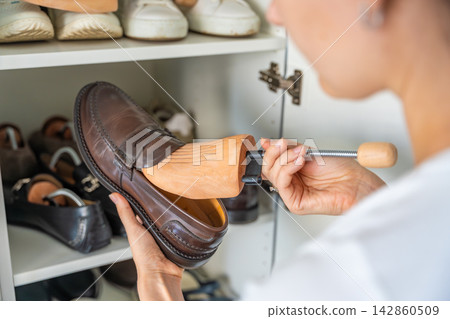 Person adjusting a wooden shoe tree inside a brown leather loafer. Care and preservation extend footwear lifespan and organization. Person adjusting a wooden shoe tree inside a brown leather loafer. Care and preservation extend footwear lifespan and organization. 142860509