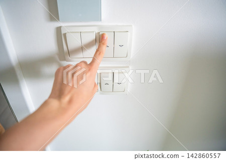 Hand pressing wall light switch in modern home interior. Energy saving and smart home control concept Hand pressing wall light switch in modern home interior. Energy saving and smart home control concept 142860557