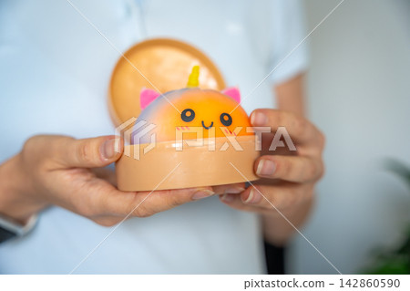 Woman opening container with cute unicorn squishy bun toy. Stress relief toy and sensory fidget concept Woman opening container with cute unicorn squishy bun toy. Stress relief toy and sensory fidget concept 142860590
