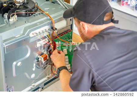 Appliance technician replacing faulty electronic control board inside electric oven. Home appliance repair and component replacement concept Appliance technician replacing faulty electronic control board inside electric oven. Home appliance repair and component replacement concept 142860592