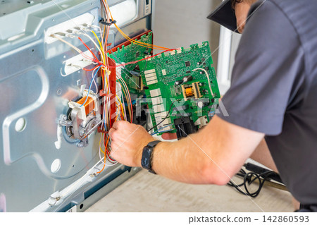 Appliance technician replacing faulty electronic control board inside electric oven. Home appliance repair and component replacement concept 142860593