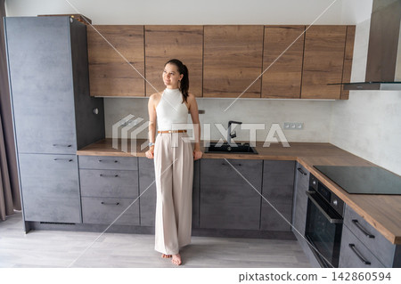 Young woman standing in furnished resale apartment kitchen after property purchase. Secondary housing and real estate investment concept Young woman standing in furnished resale apartment kitchen after property purchase. Secondary housing and real estate investment concept 142860594