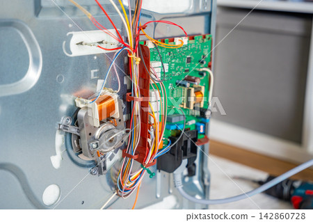 Close up view of internal electronic components inside disassembled electric oven during repair. Appliance diagnostics and professional maintenance service concept Close up view of internal electronic components inside disassembled electric oven during repair. Appliance diagnostics and professional maintenance service concept 142860728