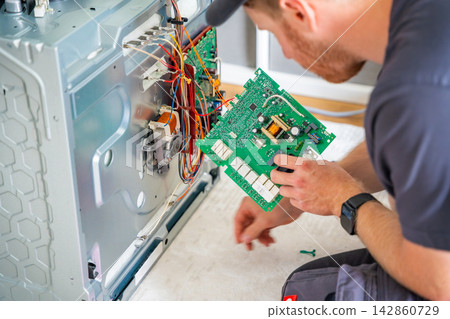 Technician replacing electronic control board inside disassembled electric oven during repair. Appliance maintenance and professional service concept 142860729