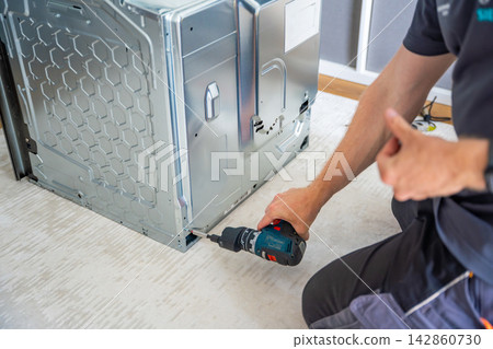 Removing protective panel from electric oven to inspect electronic components. Appliance troubleshooting concept Removing protective panel from electric oven to inspect electronic components. Appliance troubleshooting concept 142860730
