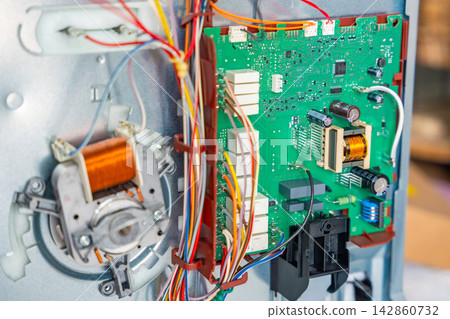 Close up view of internal electronic components inside disassembled electric oven during repair. Appliance diagnostics and professional maintenance service concept Close up view of internal electronic components inside disassembled electric oven during repair. Appliance diagnostics and professional maintenance service concept 142860732