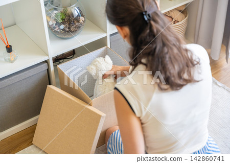 Young woman taking old stuffed toy from storage box in home interior. Home organization and decluttering with childhood memories concept 142860741