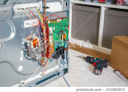 Close up view of internal electronic components inside disassembled electric oven during repair. Appliance diagnostics and professional maintenance service concept Close up view of internal electronic components inside disassembled electric oven during repair. Appliance diagnostics and professional maintenance service concept 142860853
