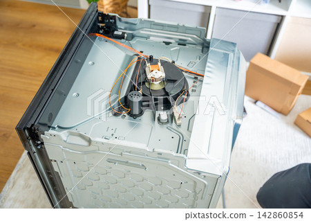 Built in electric oven with removed top panel during repair process at home. Household appliance maintenance and professional repair service concept Built in electric oven with removed top panel during repair process at home. Household appliance maintenance and professional repair service concept 142860854