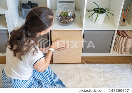 Young woman storing fabric box in minimalist shelf unit at home. Calm interior and sustainable organization concept Young woman storing fabric box in minimalist shelf unit at home. Calm interior and sustainable organization concept 142860867