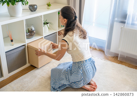 Young woman pulling storage box from shelving system in home interior. Home organization and decluttering routine concept Young woman pulling storage box from shelving system in home interior. Home organization and decluttering routine concept 142860873