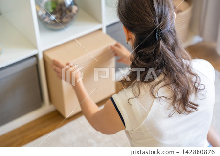 Young woman pulling storage box from shelving system in home interior. Home organization and decluttering routine concept 142860876