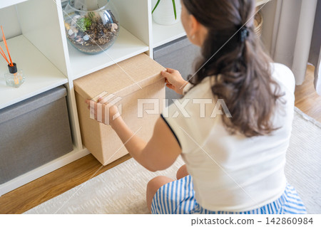 Young woman pulling storage box from shelving system in home interior. Home organization and decluttering routine concept Young woman pulling storage box from shelving system in home interior. Home organization and decluttering routine concept 142860984