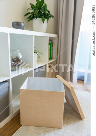 Open storage box near shelving system in organized home interior. Home organization and decluttering lifestyle concept Open storage box near shelving system in organized home interior. Home organization and decluttering lifestyle concept 142860985