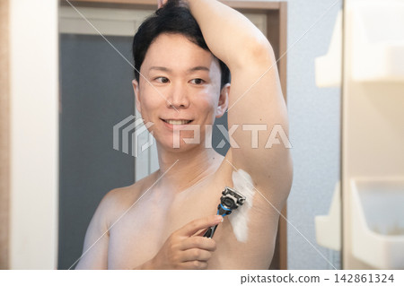 一名男子在家中浴室洗手台旁修剪腋毛。 一名男子在家中浴室洗手台旁修剪腋毛。 142861324