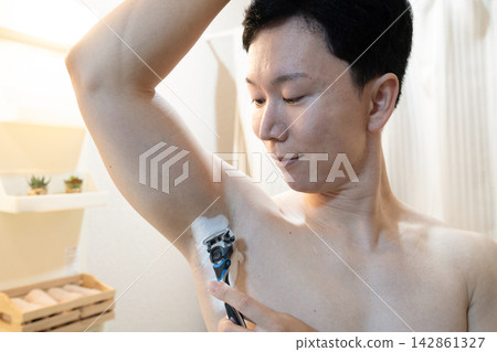 一名男子在家中浴室洗手台旁修剪腋毛。 142861327