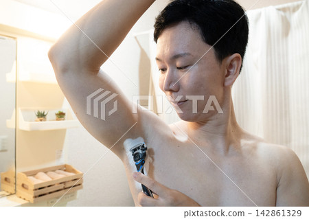 一名男子在家中浴室洗手台旁修剪腋毛。 一名男子在家中浴室洗手台旁修剪腋毛。 142861329
