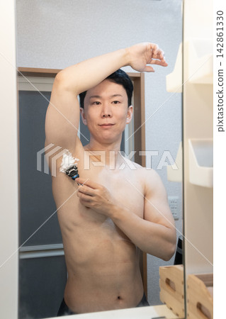 一名男子在家中浴室洗手台旁修剪腋毛。 一名男子在家中浴室洗手台旁修剪腋毛。 142861330