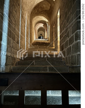 A solemn stone corridor bathed in sunlight and a staircase leading upwards. A solemn stone corridor bathed in sunlight and a staircase leading upwards. 142861692