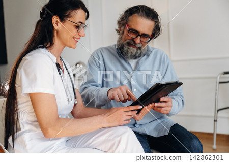Female healthcare professional in white scrubs discusses medical information with male patient using tablet in modern clinic setting with bright interior Female healthcare professional in white scrubs discusses medical information with male patient using tablet in modern clinic setting with bright interior 142862301