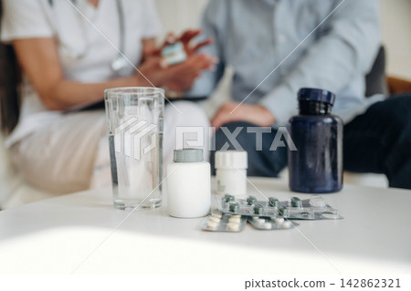 Medical consultation scene with healthcare professional discussing medication options with patient, various pill bottles and a glass of water on the table Medical consultation scene with healthcare professional discussing medication options with patient, various pill bottles and a glass of water on the table 142862321