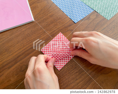 A Japanese woman's hands folding origami on a wooden table. A Japanese woman's hands folding origami on a wooden table. 142862978