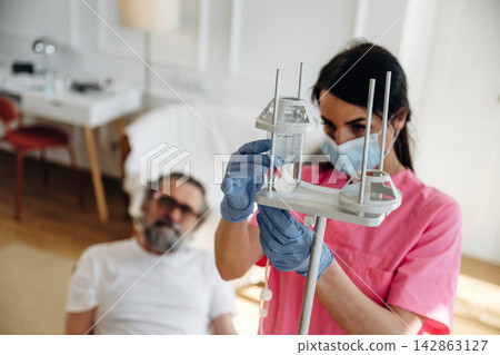 Female nurse in pink scrubs prepares IV drip for patient in a home care setting with modern furnishings and a comfortable atmosphere Female nurse in pink scrubs prepares IV drip for patient in a home care setting with modern furnishings and a comfortable atmosphere 142863127