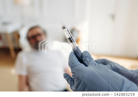 Healthcare professional in blue gloves holds insulin syringe while patient reclines on examination table in bright medical office with soft lighting and minimal decor Healthcare professional in blue gloves holds insulin syringe while patient reclines on examination table in bright medical office with soft lighting and minimal decor 142863259