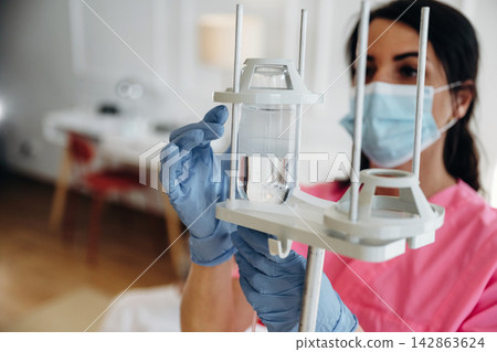 Female healthcare professional in pink scrubs adjusts IV drip with clear fluid in a medical facility, bright interior with furniture visible in the background Female healthcare professional in pink scrubs adjusts IV drip with clear fluid in a medical facility, bright interior with furniture visible in the background 142863624