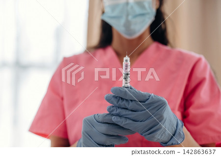 Healthcare professional in pink scrubs holds a syringe with insulin, wearing blue gloves and a face mask, in a well-lit medical environment with soft background Healthcare professional in pink scrubs holds a syringe with insulin, wearing blue gloves and a face mask, in a well-lit medical environment with soft background 142863637