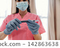 Healthcare professional in pink scrubs wearing gloves and a mask holds an insulin pen for diabetes management in a well-lit medical environment 142863638
