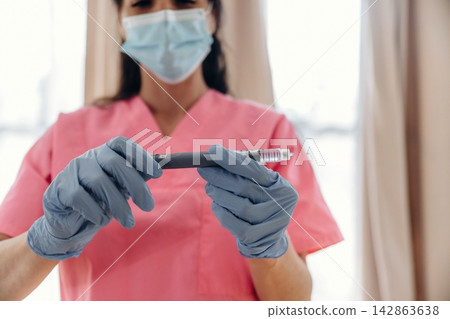 Healthcare professional in pink scrubs wearing gloves and a mask holds an insulin pen for diabetes management in a well-lit medical environment Healthcare professional in pink scrubs wearing gloves and a mask holds an insulin pen for diabetes management in a well-lit medical environment 142863638