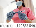 Healthcare professional in pink scrubs prepares insulin syringe for diabetes treatment, wearing blue gloves and a surgical mask in a clinical setting with natural light 142863640