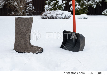 Winter felt boots and snow shovel in snowy garden Winter felt boots and snow shovel in snowy garden 142863848