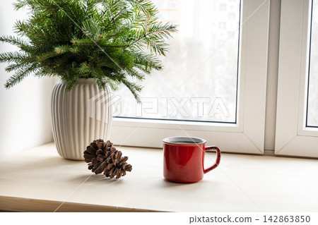 Red mug with pine cone on windowsill in winter Red mug with pine cone on windowsill in winter 142863850
