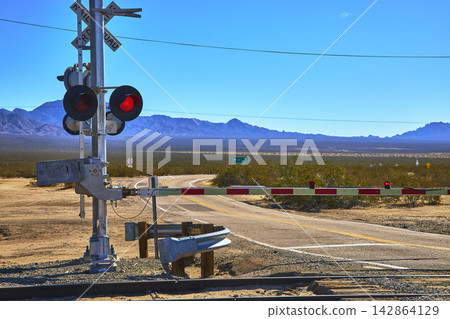 Railroad Crossing Barrier and Desert Road in Mojave Landscape California Railroad Crossing Barrier and Desert Road in Mojave Landscape California 142864129